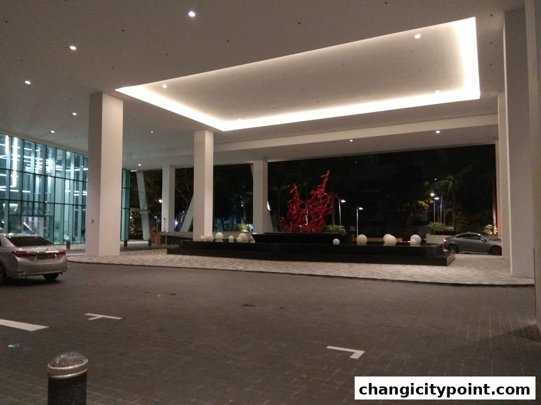 Modern building entrance with a sculpture and water feature at night.