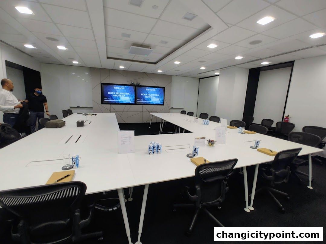 A modern conference room with a U-shaped table, chairs, and screens displaying a welcome message.
