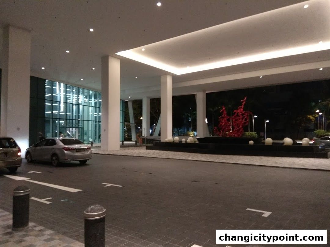Modern building entrance with cars, modern sculpture, and water feature.