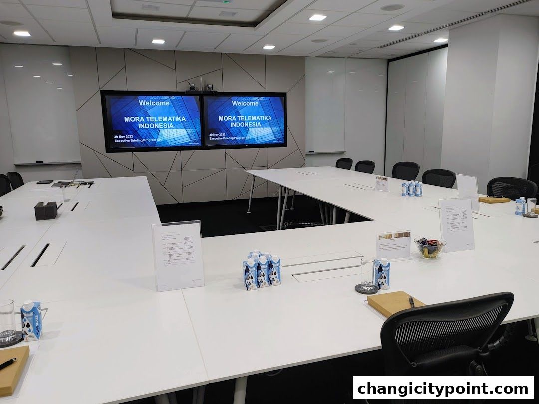 A modern conference room with a large U-shaped table, screens, and chairs.