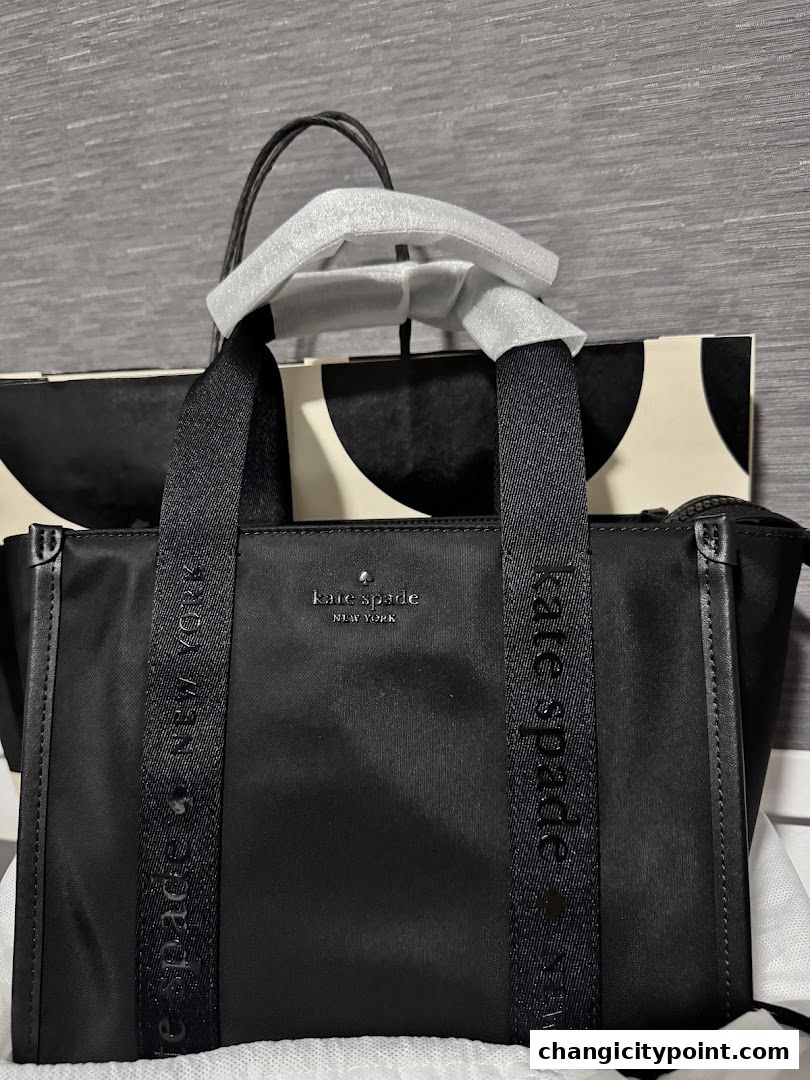 A black Kate Spade New York tote bag with branded straps and a shopping bag in the background.