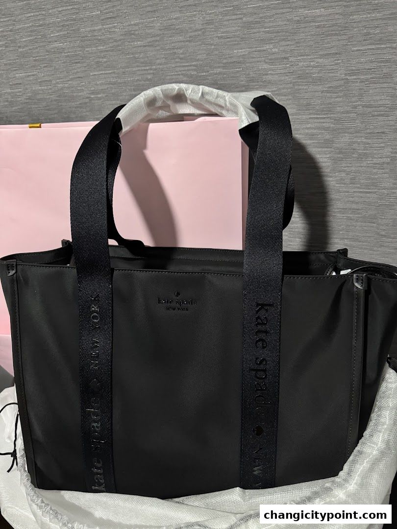 A black Kate Spade tote bag with branded straps and a pink box in the background.