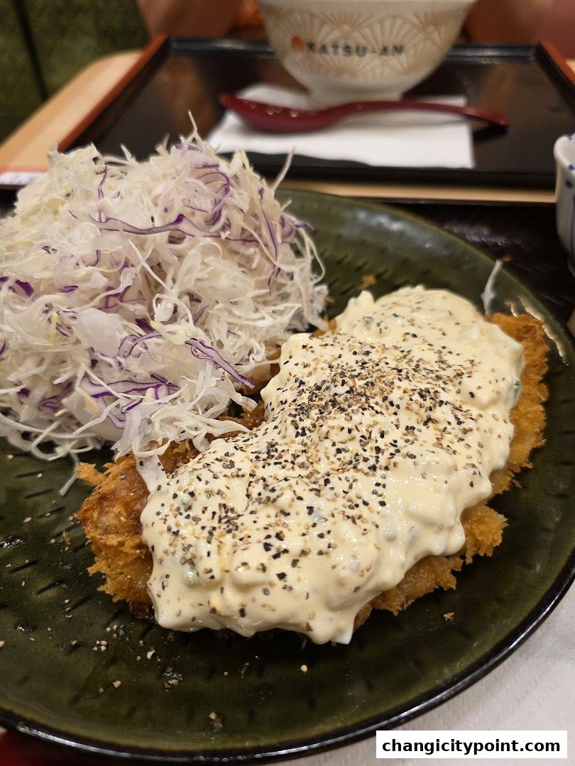 A close-up of a katsu dish with shredded cabbage and a creamy sauce.