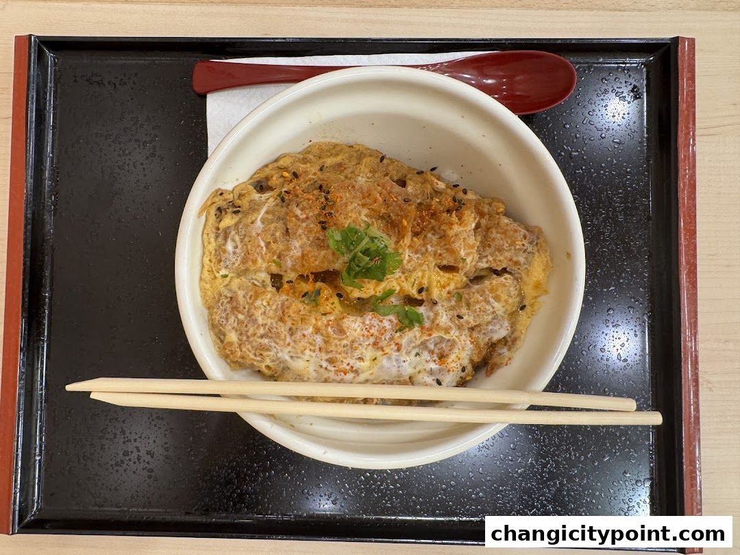 A delicious bowl of katsudon served with chopsticks and a spoon on a tray.