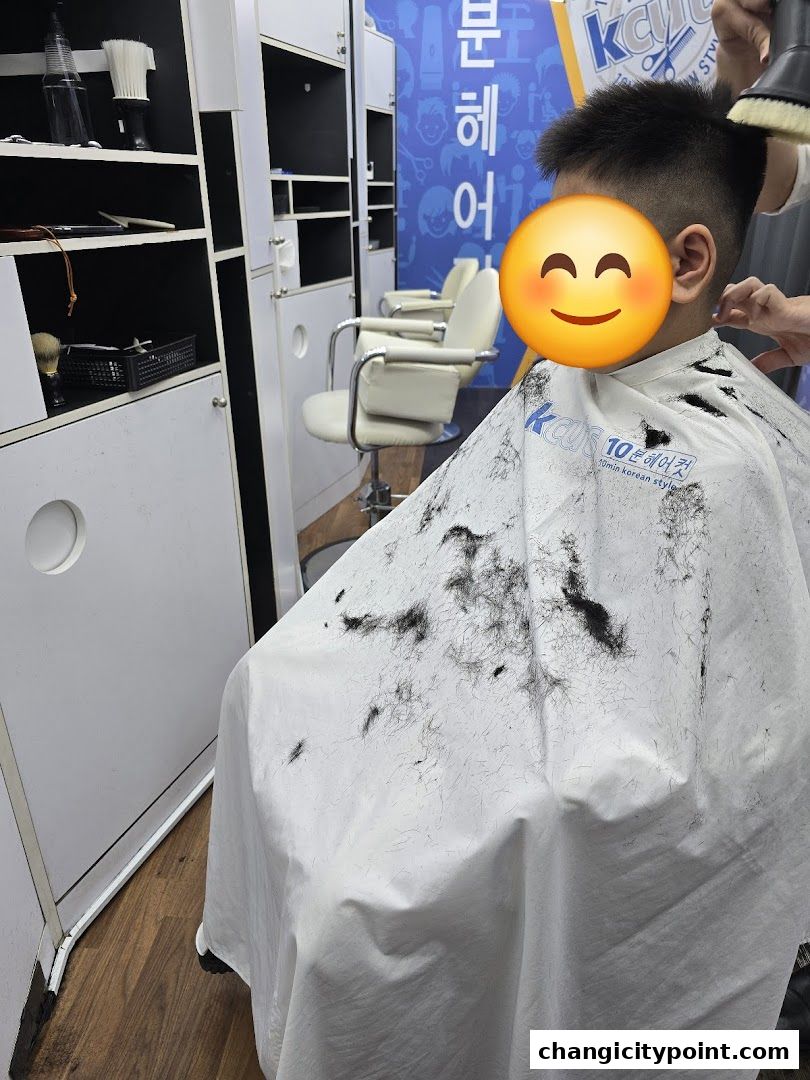 A child getting a haircut at a salon, with hair clippings on the cape.