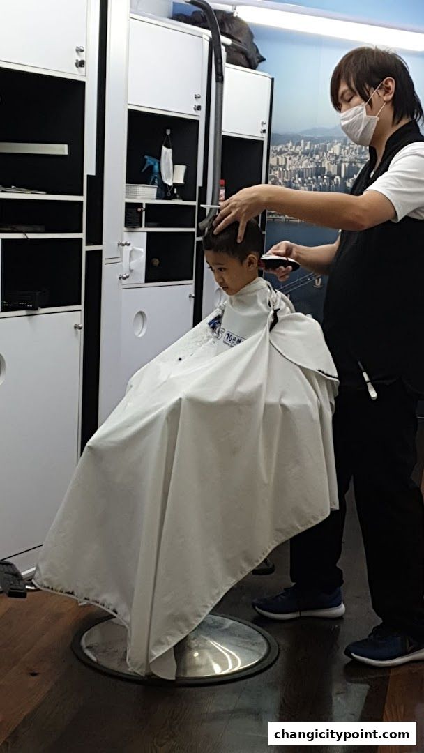 A barber cuts a young boy's hair in a clean, modern salon.