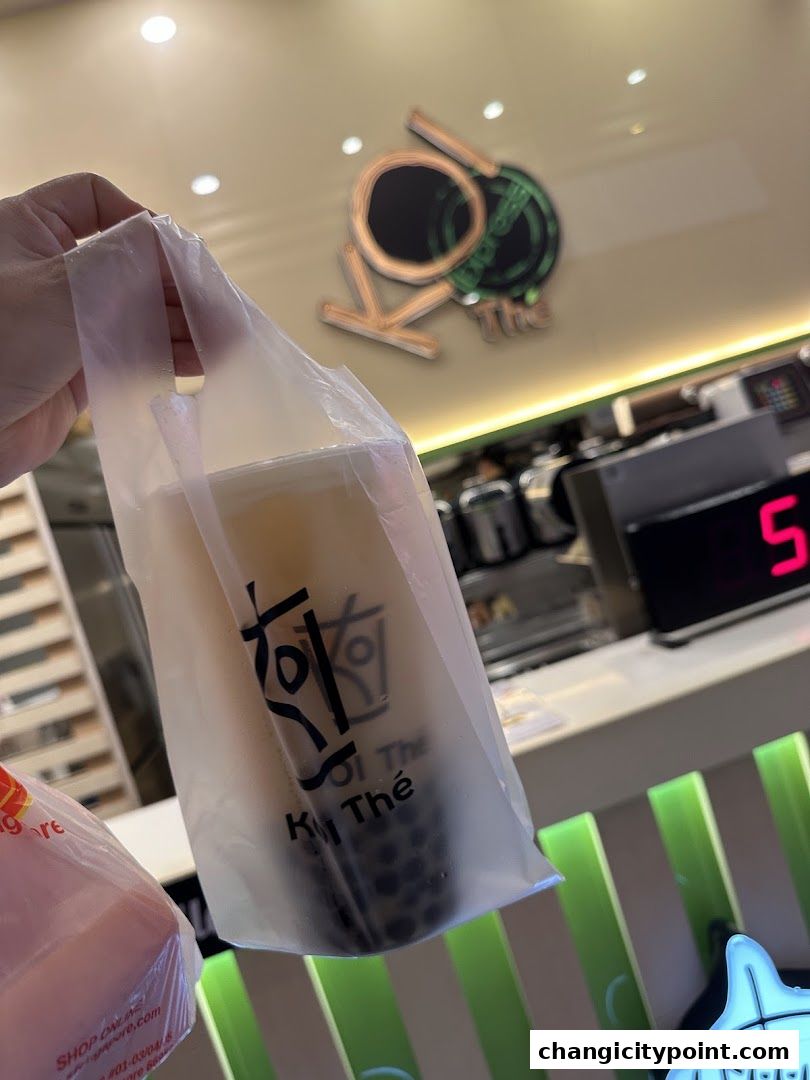 A hand holds a KOI Thé bubble tea bag in front of the shop's logo.