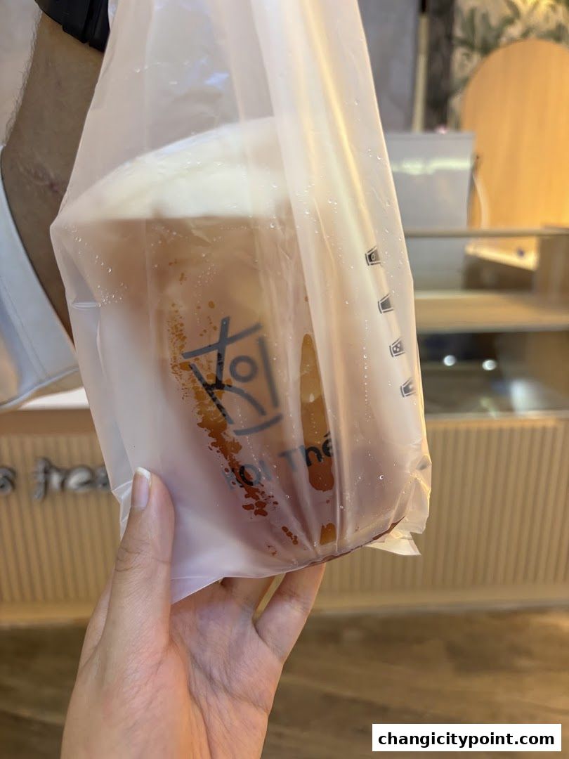 A hand holds a plastic bag with a drink from KOI Express.