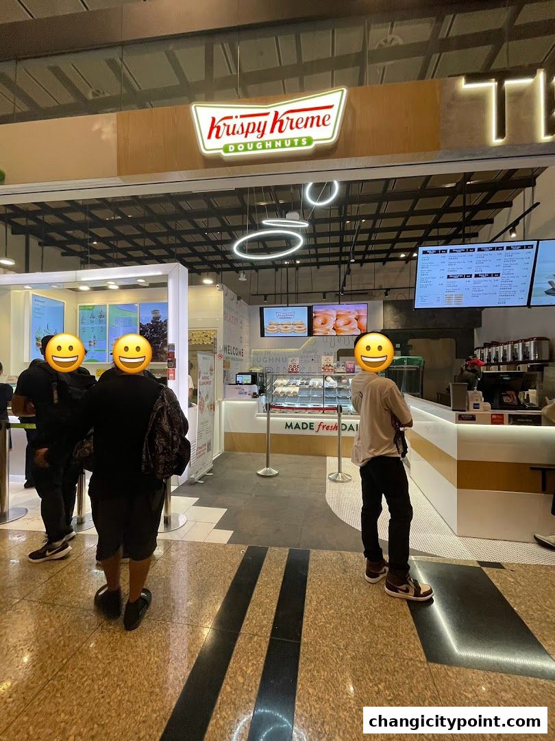 The entrance of a Krispy Kreme doughnut shop with customers and displays.