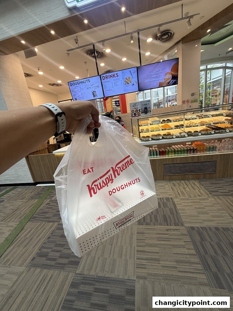 A person holds a Krispy Kreme bag with a box of doughnuts inside.