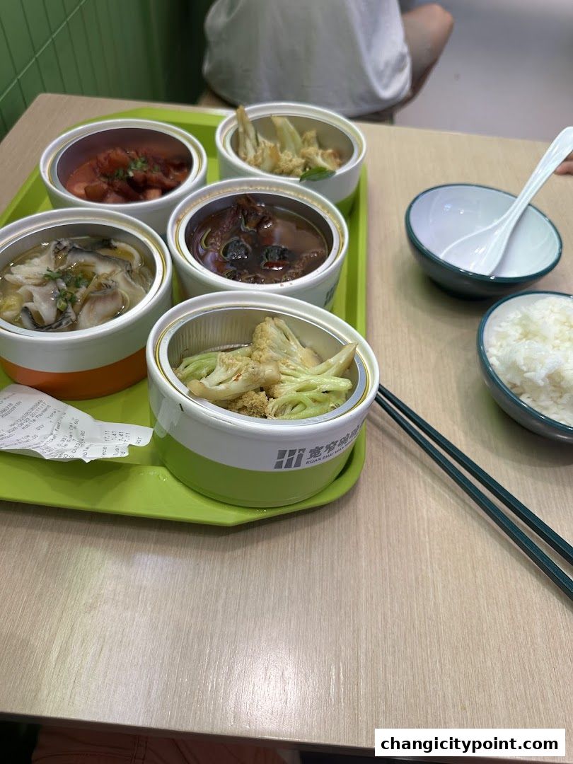 A tray of assorted Chinese dishes served in individual containers with rice and chopsticks.