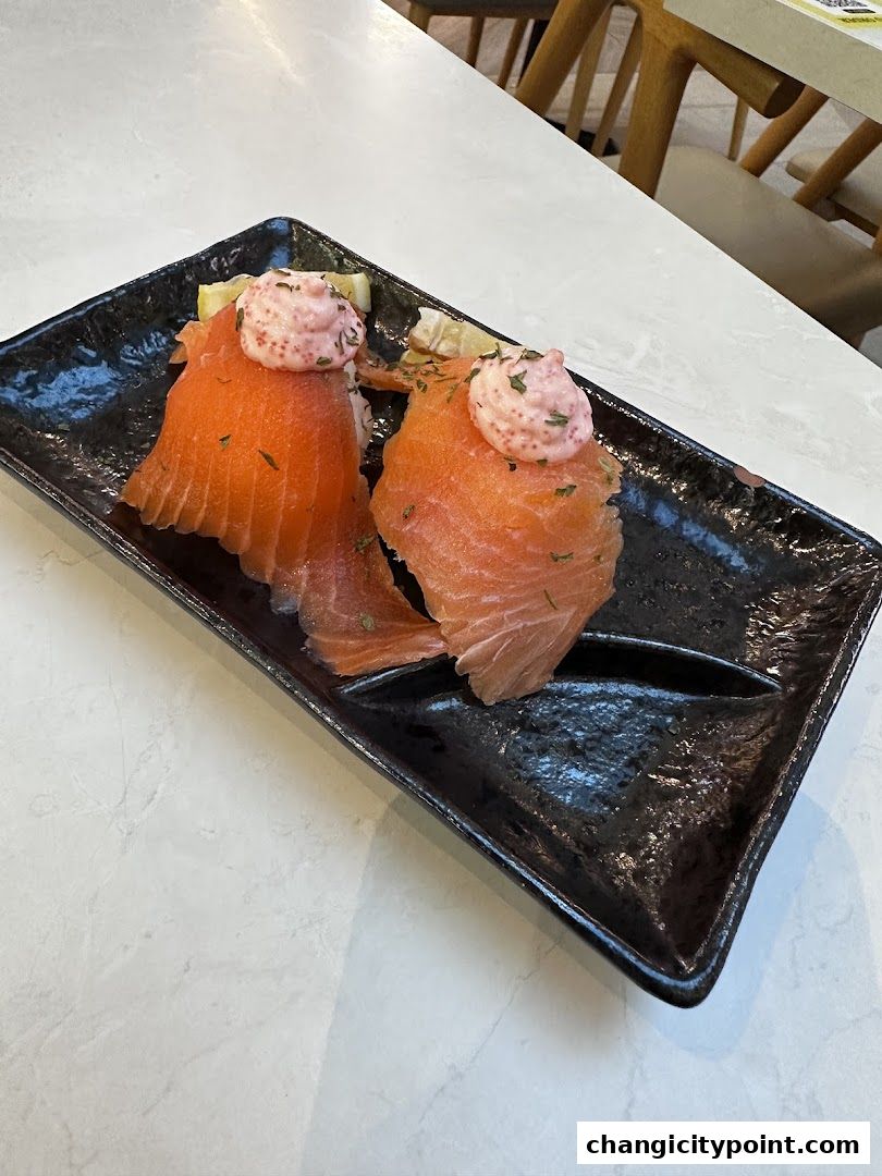 Two pieces of salmon sushi with pink sauce and herbs on a black plate.