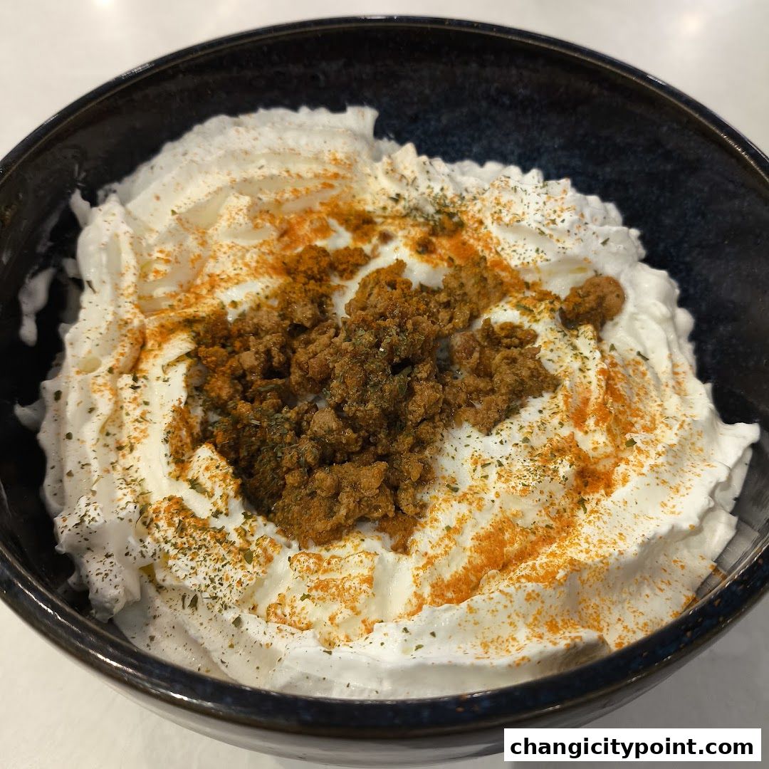 A bowl of whipped cream topped with crumbled savory ingredients and spices.