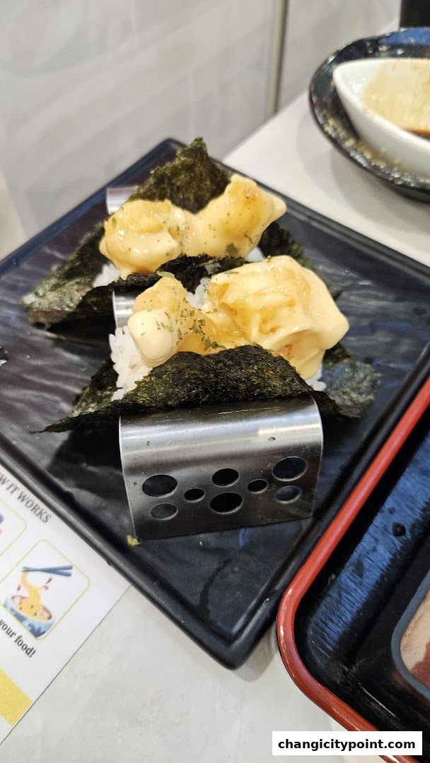 Close-up of sushi with seaweed, rice, and creamy topping on a black plate.