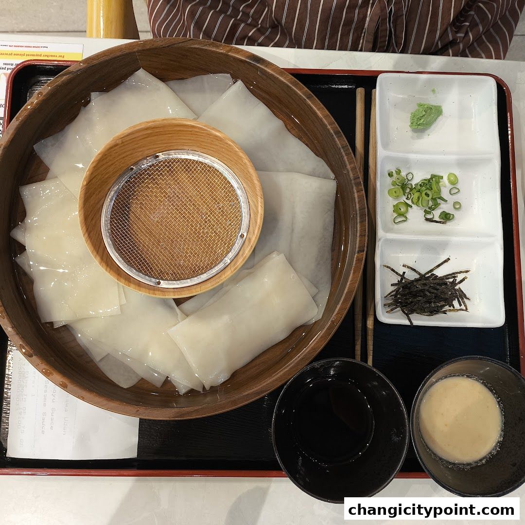 A close-up of a Japanese dish with noodles, dipping sauces, and condiments.