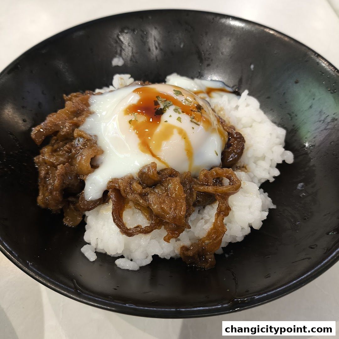 A close-up of a Japanese beef bowl with a fried egg and sauce.