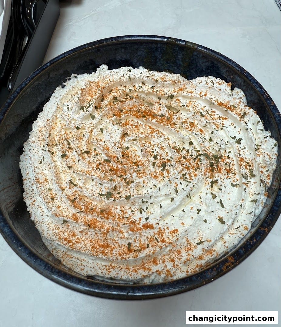 A close-up of a creamy dessert in a dark blue bowl, sprinkled with paprika and herbs.