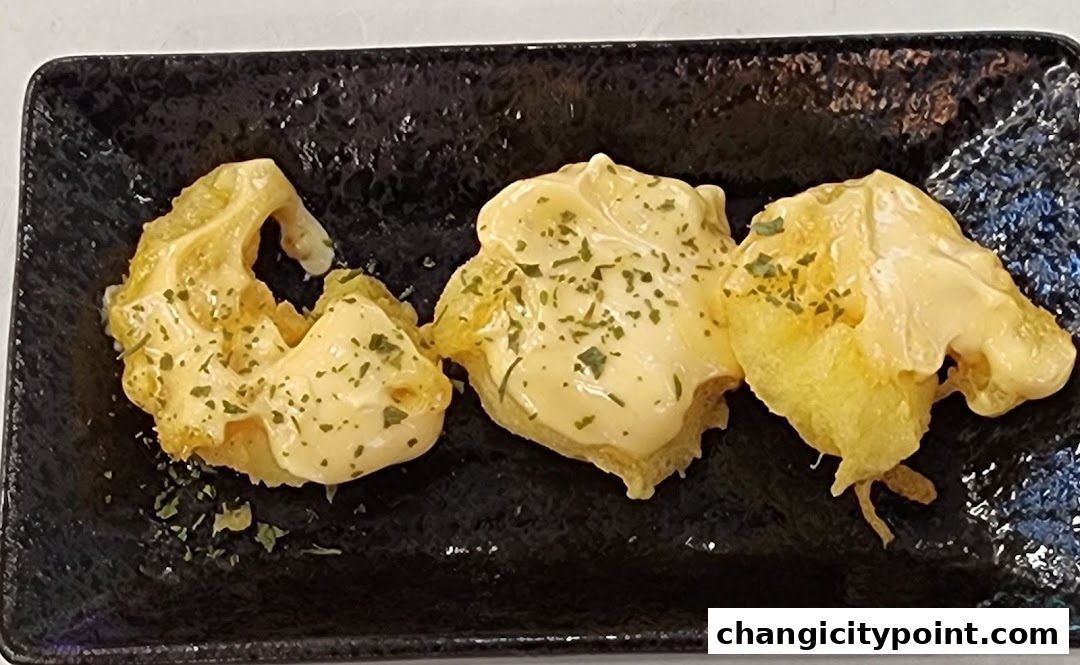 Three pieces of fried food topped with creamy sauce and herbs on a black plate.