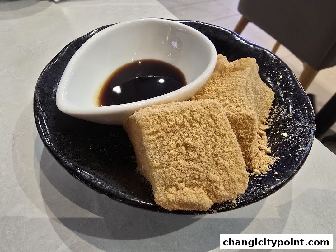 A close-up of kinako mochi with a dipping sauce on a black plate.