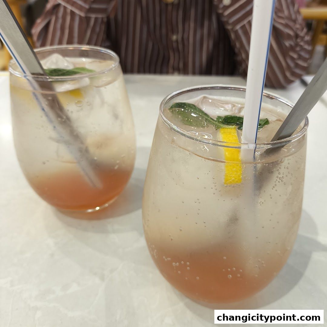 Two refreshing drinks with ice, lemon, and mint on a marble table.