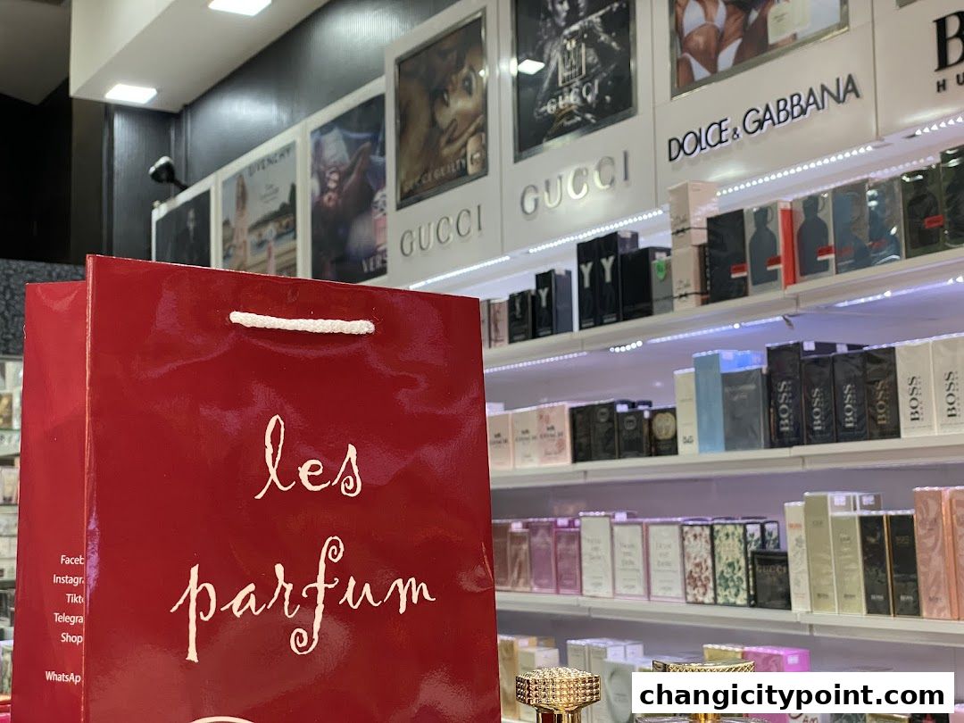 A red shopping bag with 'les parfum' logo in front of shelves stocked with perfumes.
