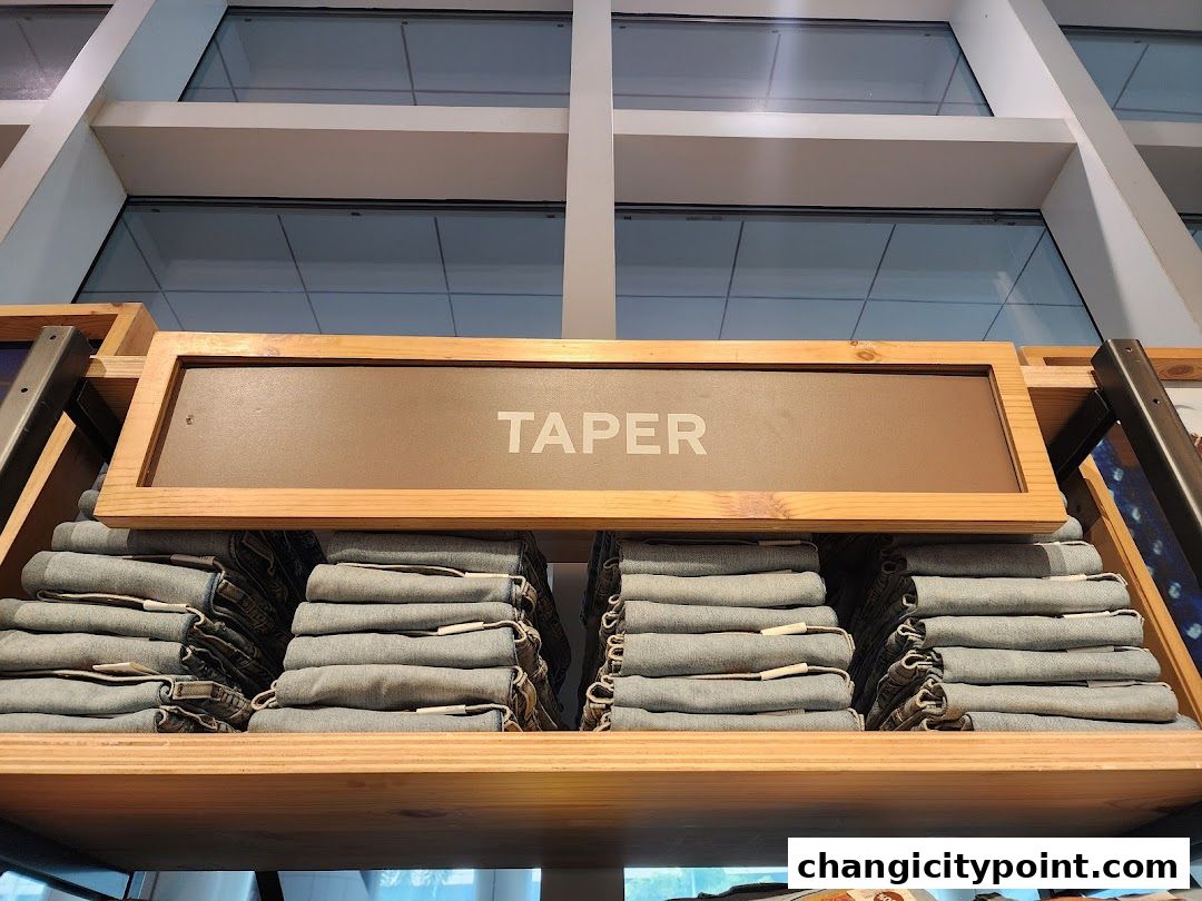 Neatly folded stacks of jeans labeled 'TAPER' on a wooden shelf.