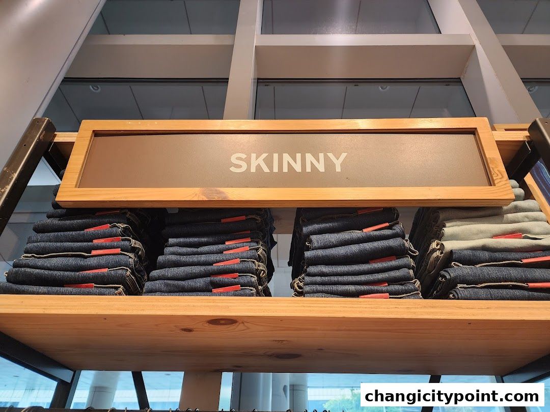 Neatly folded stacks of skinny jeans on a wooden shelf with a 'SKINNY' sign.