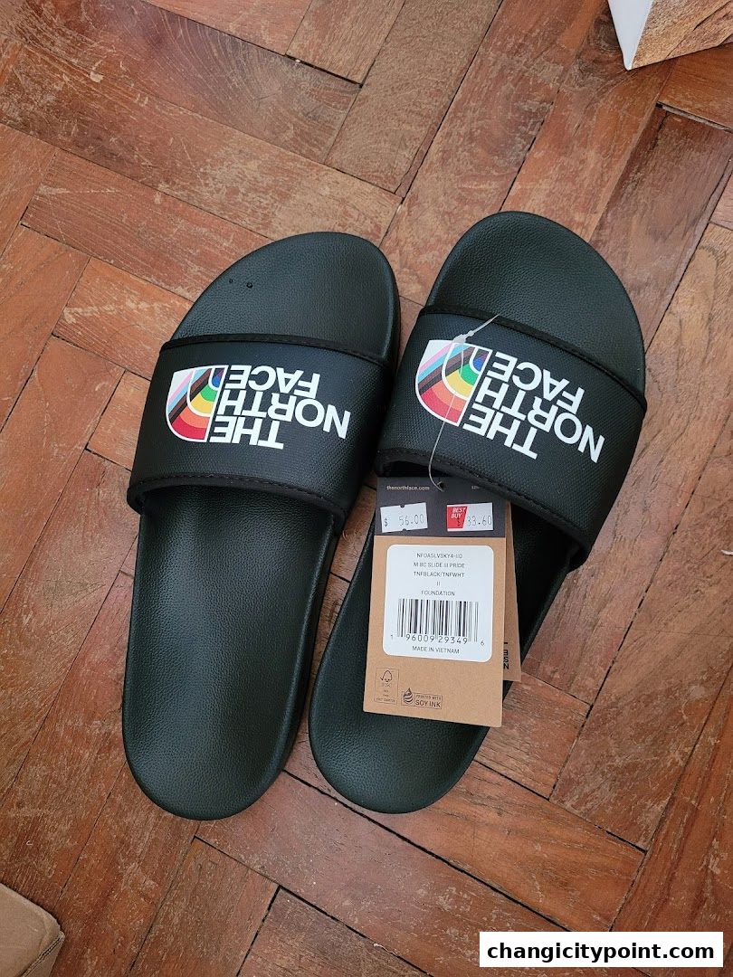 A pair of black The North Face slides with rainbow logo detail and price tags.