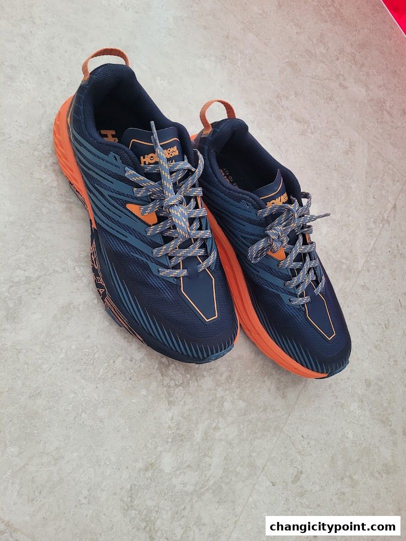 A pair of navy blue and orange Hoka running shoes are displayed on a tiled floor.
