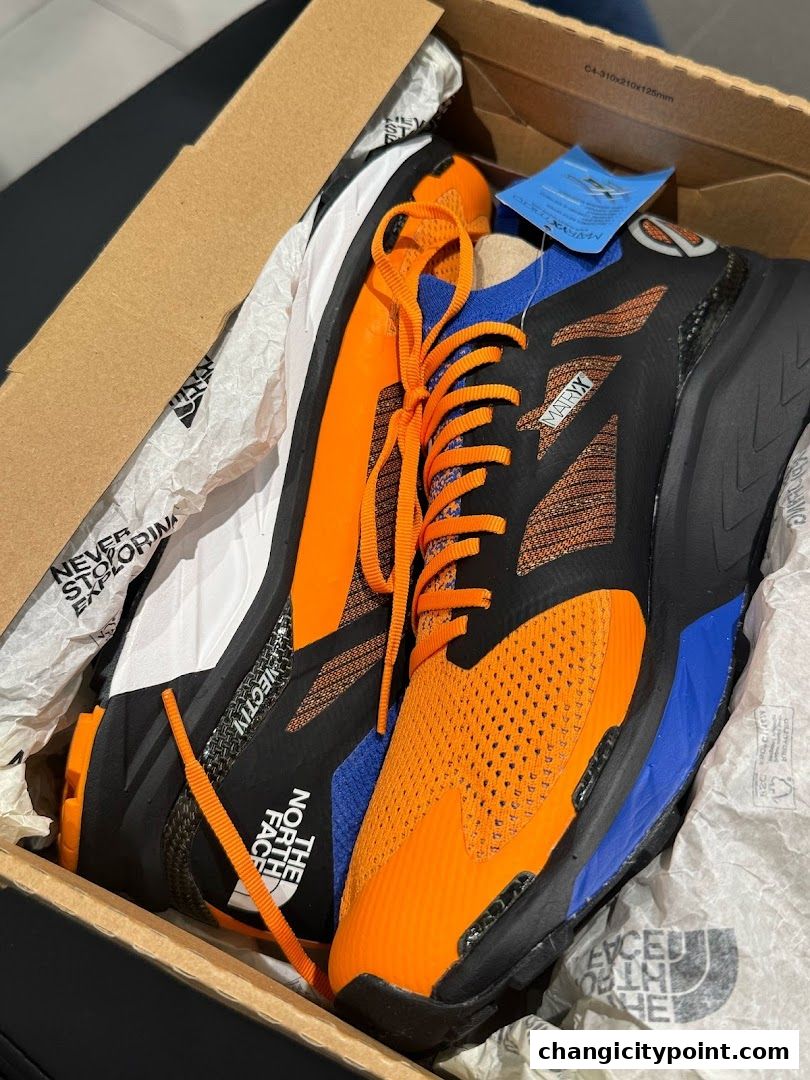 A pair of vibrant orange and black The North Face athletic shoes in a box.