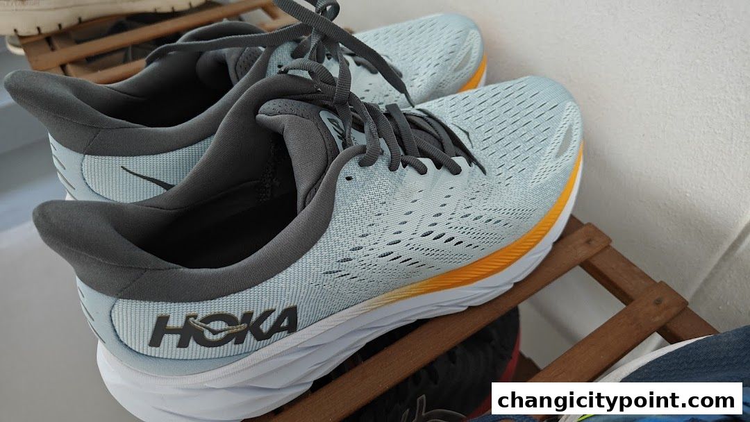 Close-up of light blue Hoka running shoes with orange accents on a wooden rack.