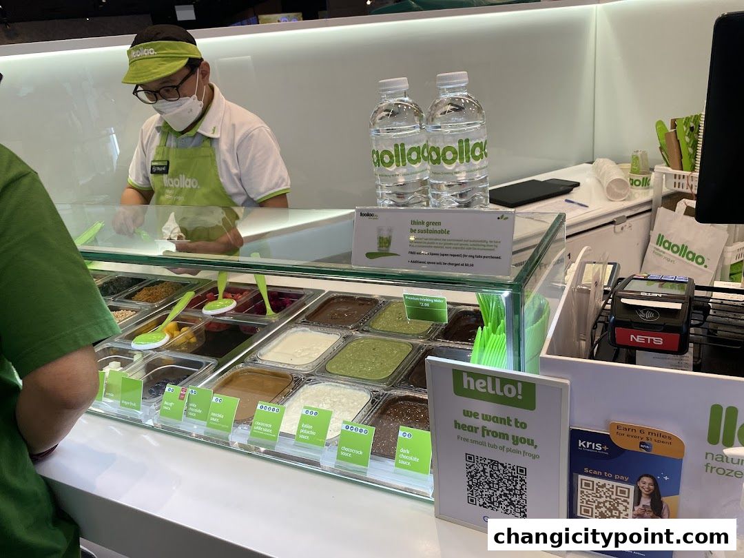 A staff member serves frozen yogurt with various toppings at a llaollao shop.