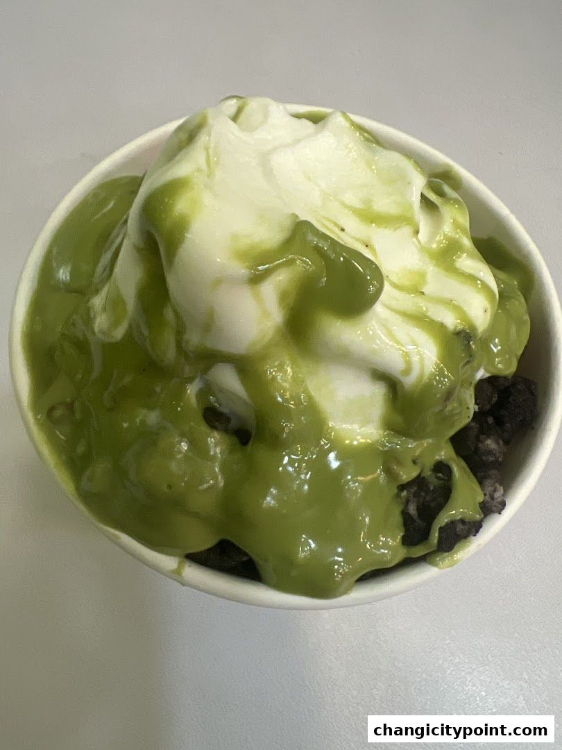 A cup of frozen yogurt topped with green sauce and cookie crumbles.