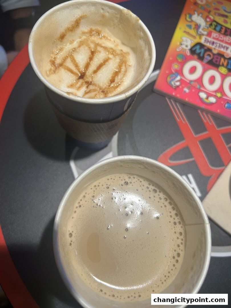 Two cups of coffee, one with latte art, sit on a table next to a colorful sticker book.