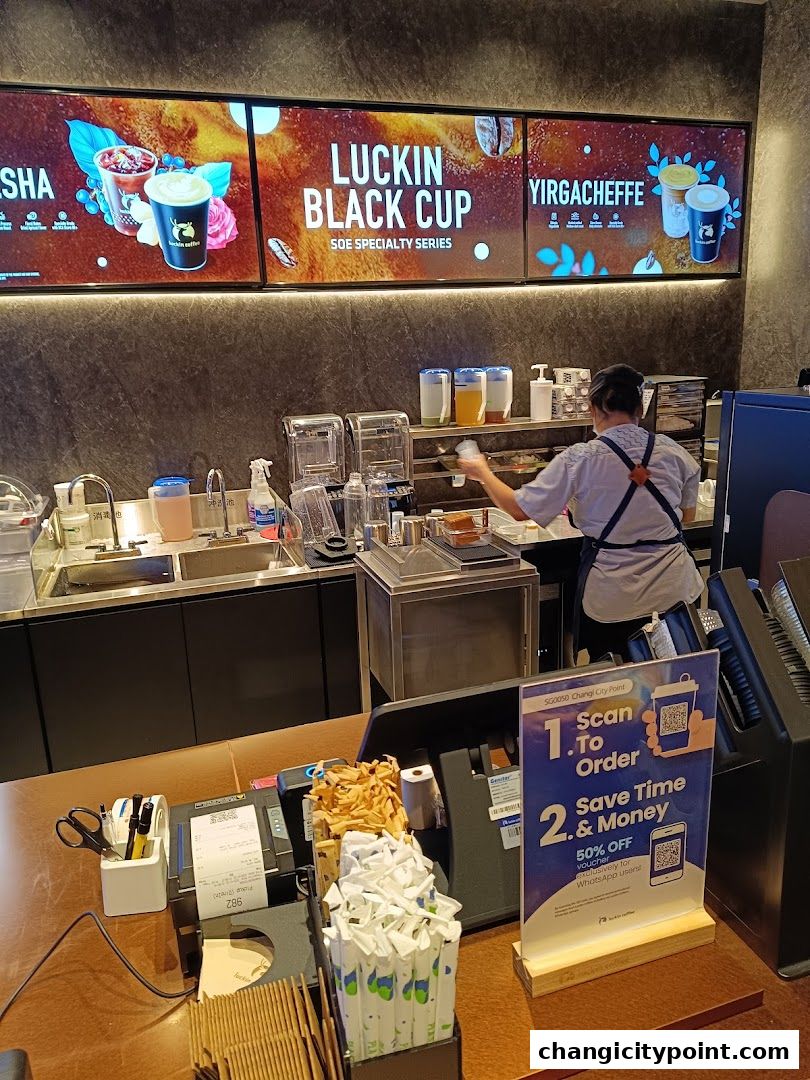 A Luckin Coffee counter with digital menus, a barista preparing drinks, and ordering information.