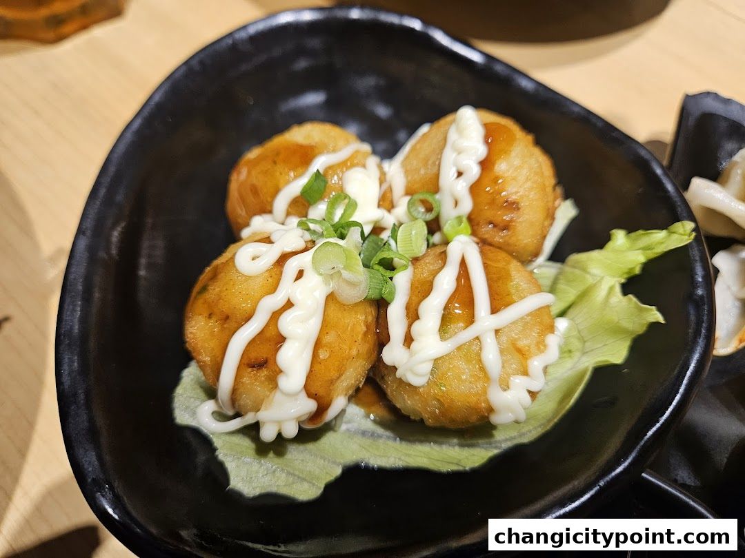 A close-up of takoyaki balls drizzled with sauce and mayonnaise on a black plate.