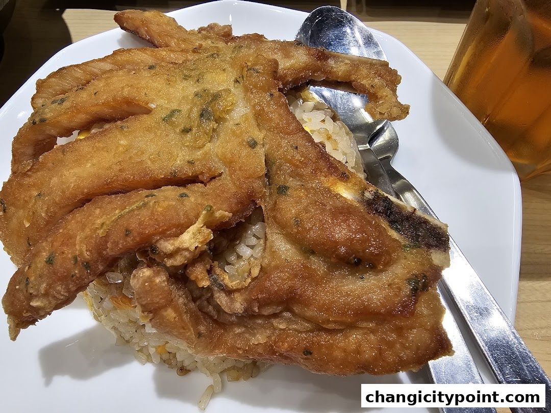 A plate of fried fish served over rice with a side of iced tea.