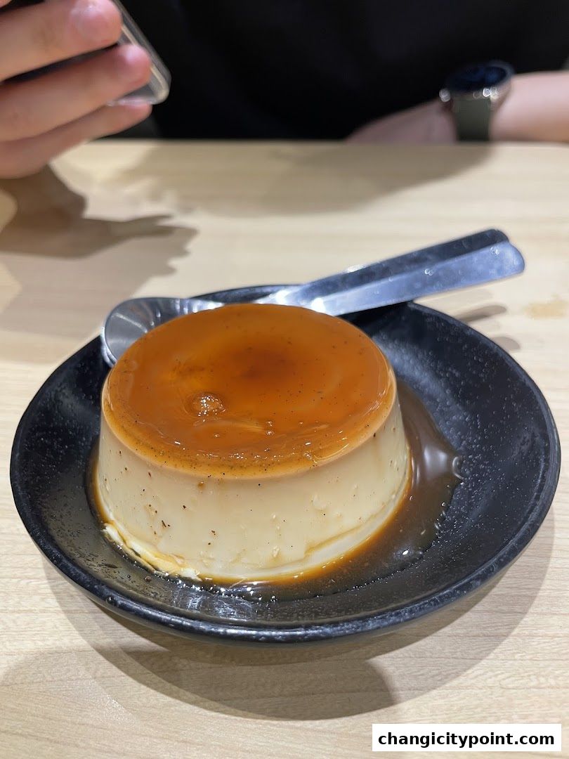 A close-up of a caramel custard dessert served on a black plate with a spoon.