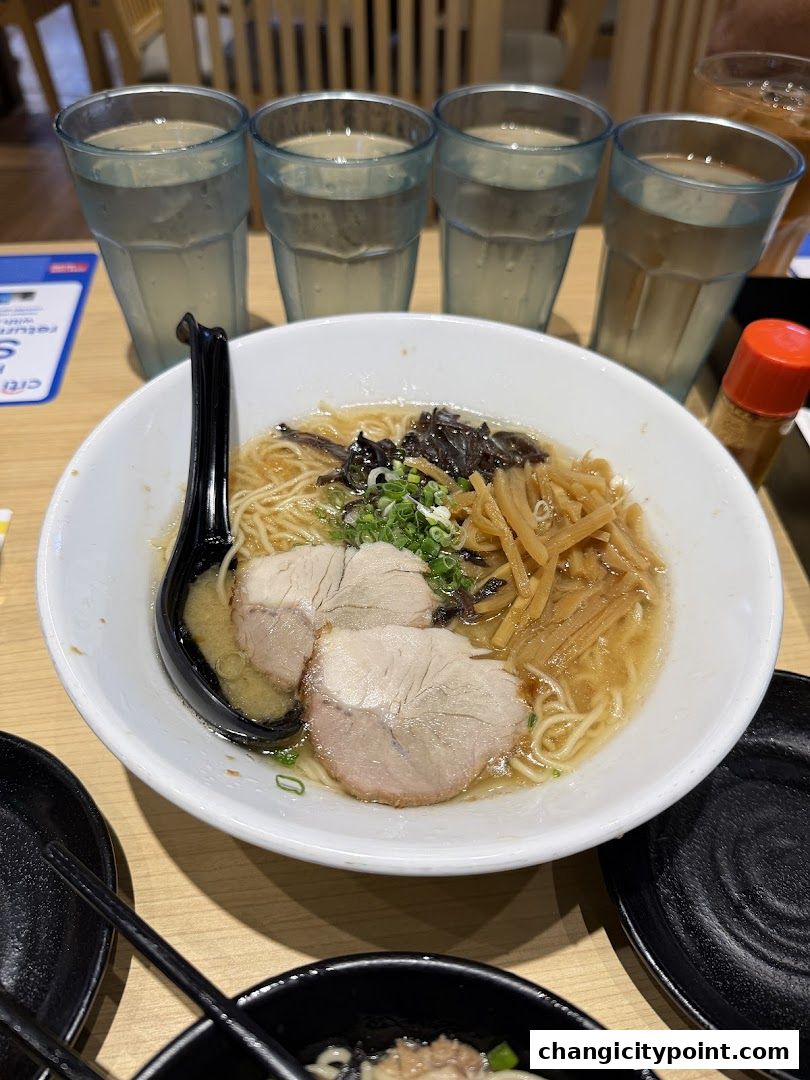 A bowl of ramen with pork slices, bamboo shoots, and green onions, served with glasses of water.