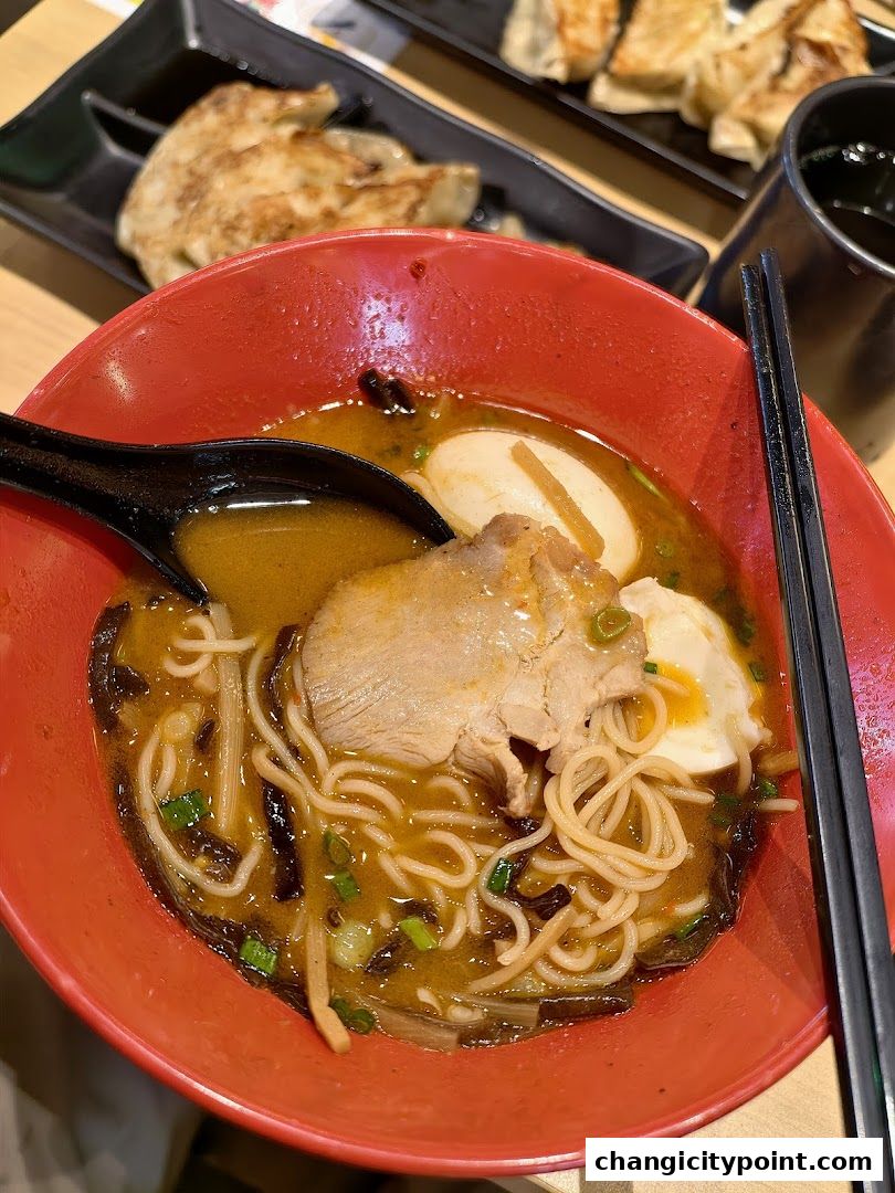 A close-up of a steaming bowl of ramen with pork, egg, and noodles, served with gyoza.