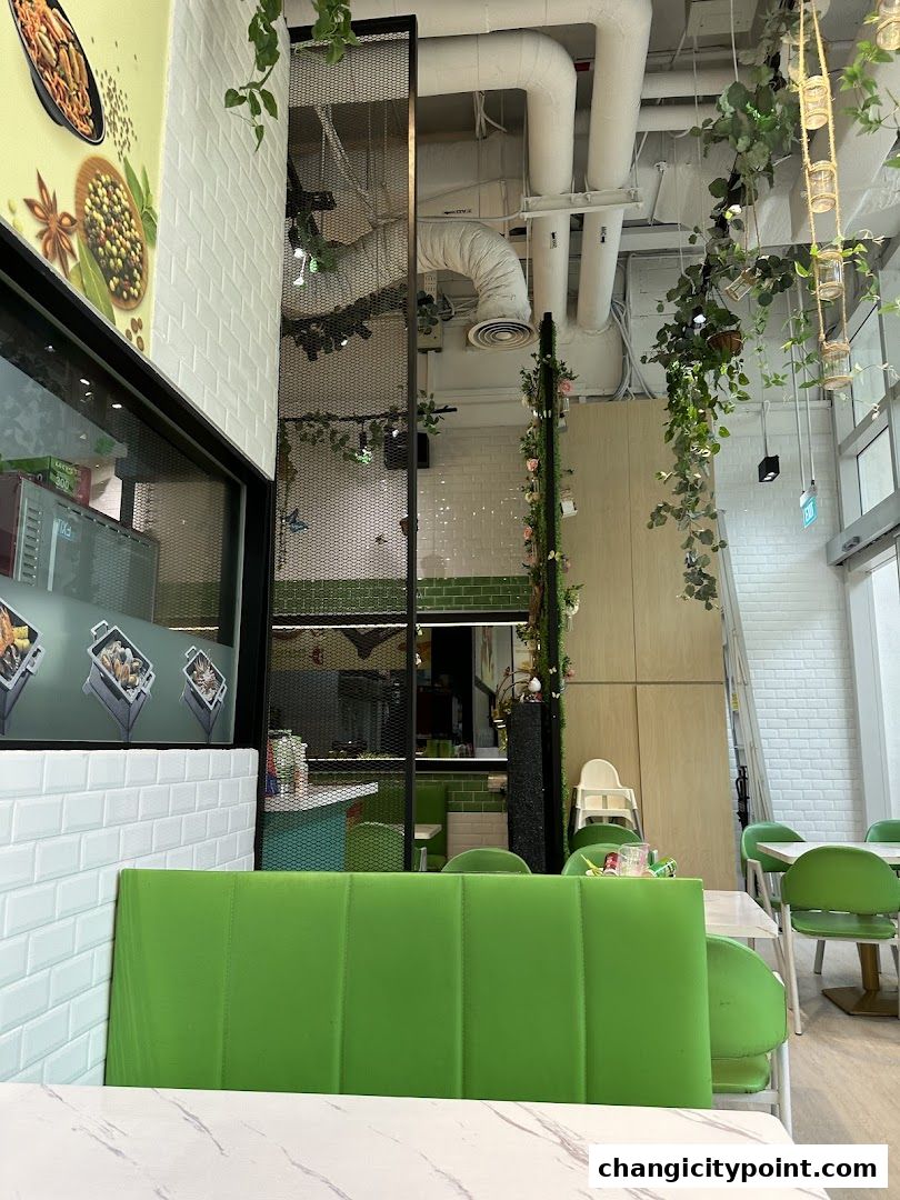 Interior view of a restaurant with green seating, plants, and exposed ceiling pipes.