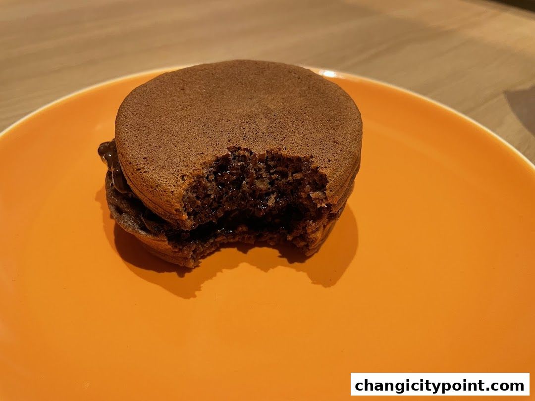 A chocolate dorayaki with a bite taken out, served on an orange plate.