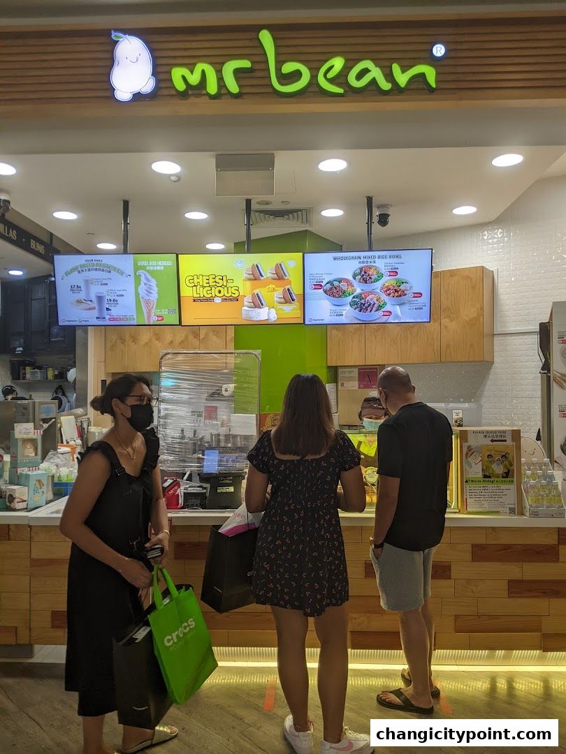 People queuing at a Mr Bean shop with digital menus displaying food and drinks.