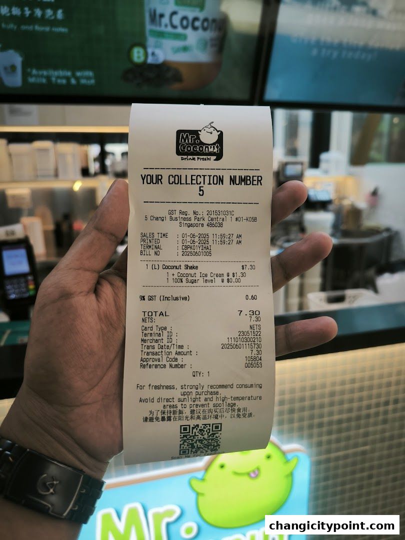A hand holds a receipt from Mr. Coconut with a blurred shop interior in the background.