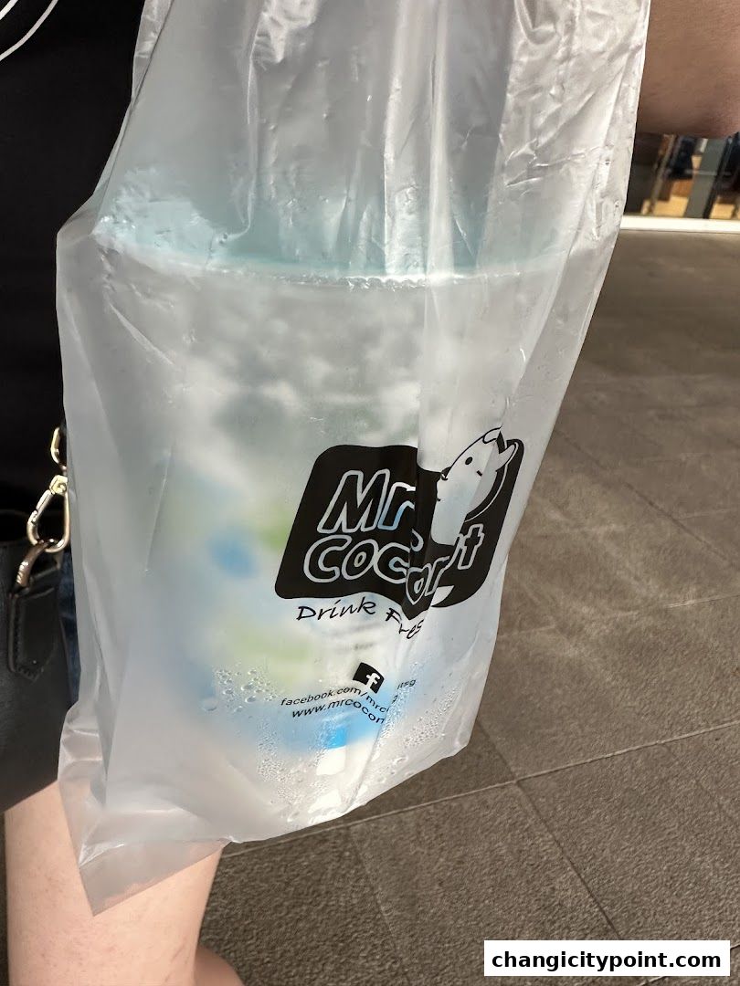 A person holding a plastic bag with a Mr. Coconut drink inside.
