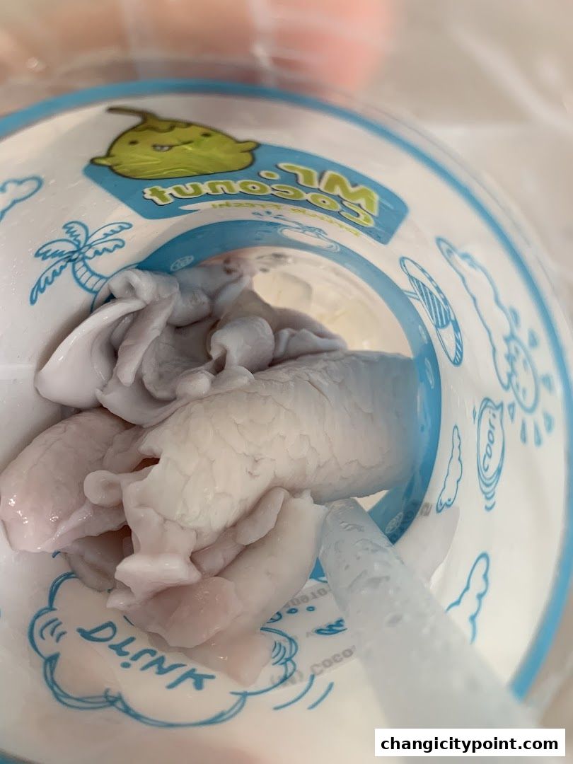 Close-up of coconut flesh inside a Mr. Coconut cup with a straw.