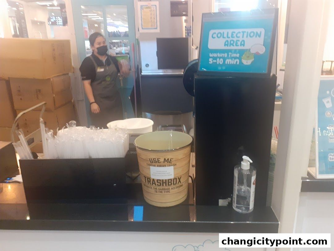 A shop counter with a trash can, hand sanitizer, and a collection area sign.