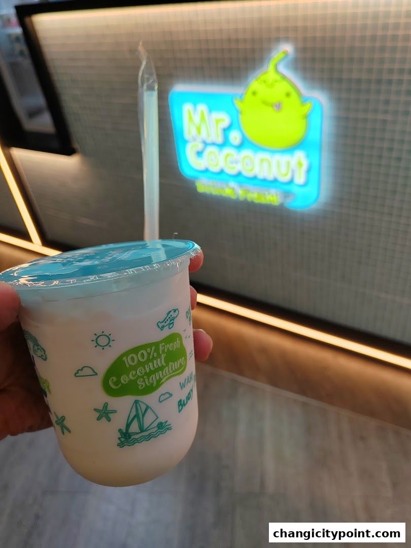 A hand holds a coconut drink with the Mr. Coconut logo in the background.