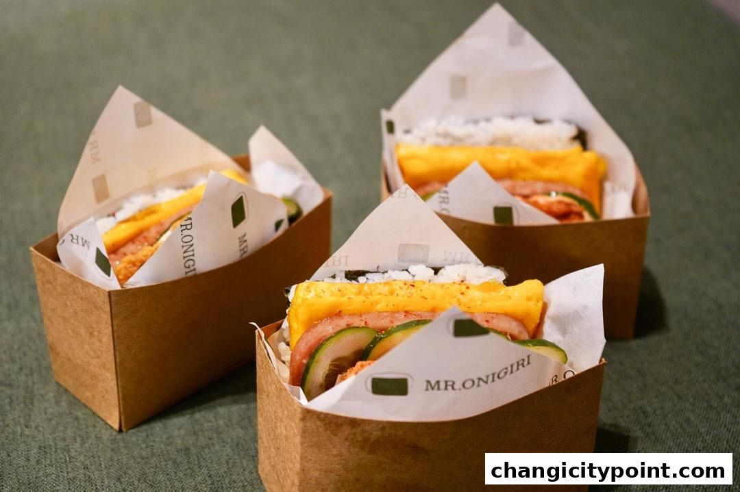 Three delicious onigiri sandwiches with egg, ham, and cucumber in brown paper packaging.