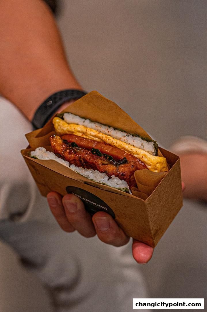 A hand holds a delicious onigiri sandwich with rice, egg, and meat filling.
